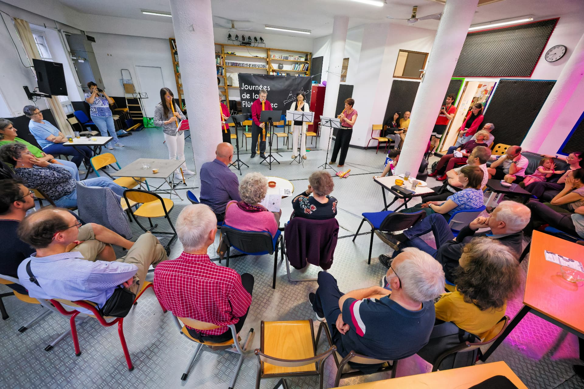 A neighbourhood audience seated in a circle around a small flute ensemble