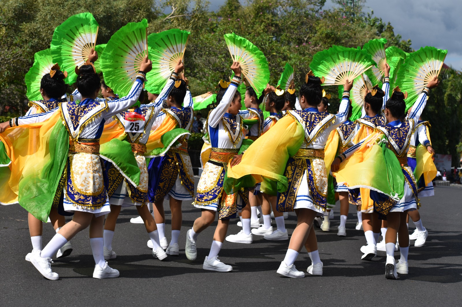 A youth troupe parading with green fans and bright costumes