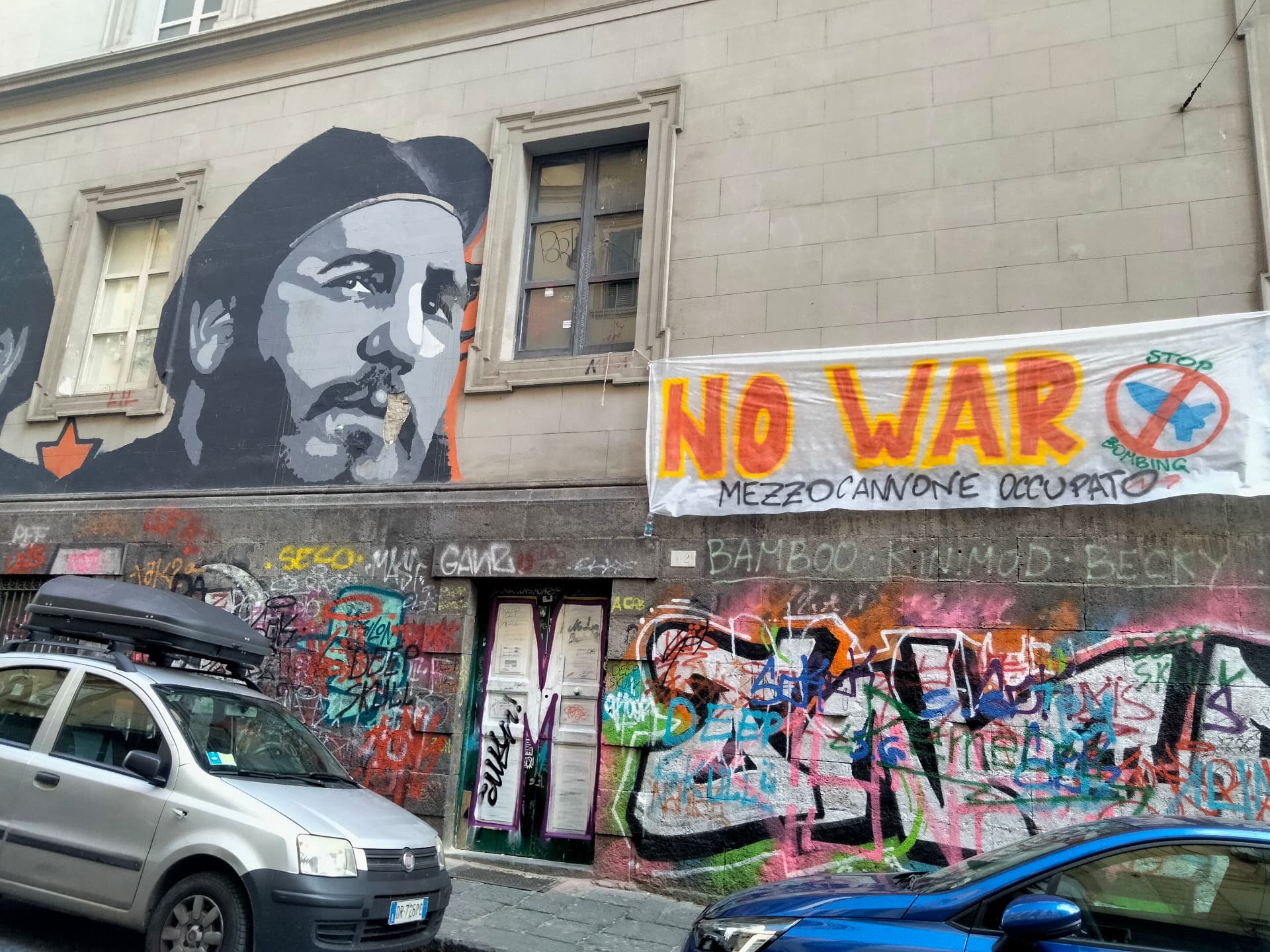 A street wall with a painted portrait and a hand-made 'No War' banner
