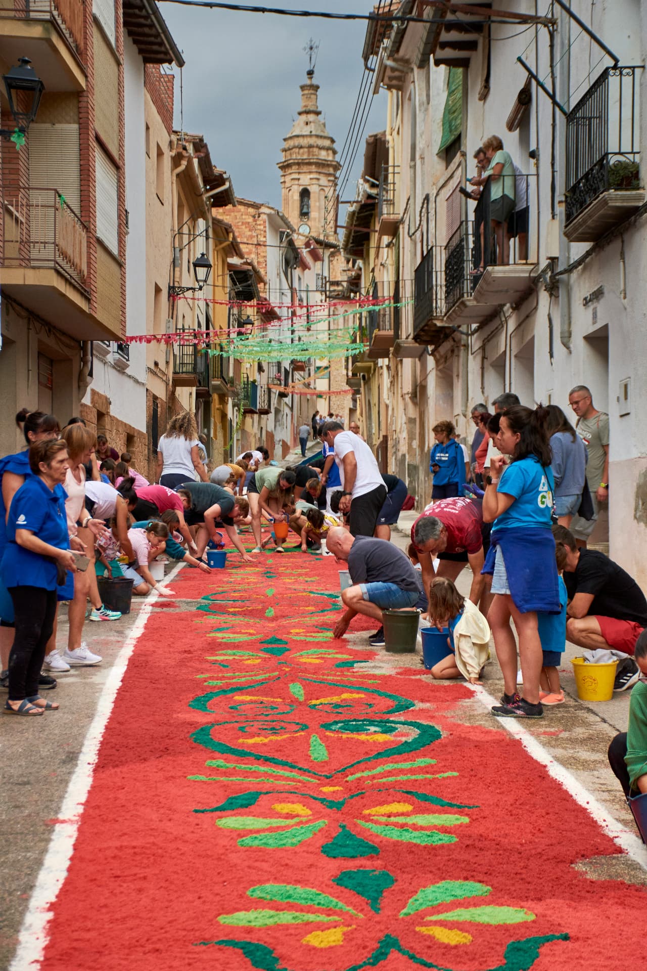 Neighbours kneeling together to lay a coloured flower carpet along a village street