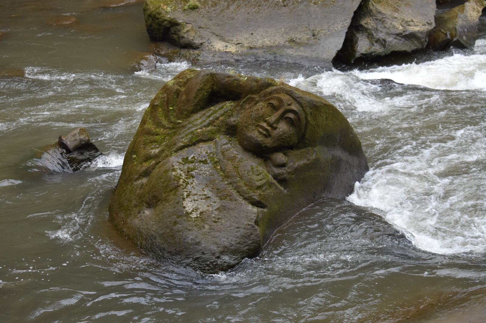 A carved stone figure resting in a flowing river